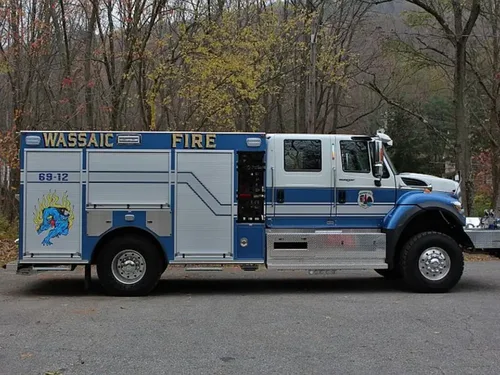 Exterior view of small fire truck showing cab, body compartments, and wheel/tire area.