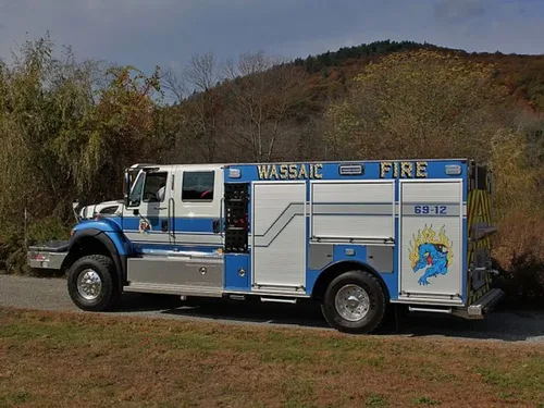 Exterior view of small fire truck showing cab, body compartments, and wheel/tire area.