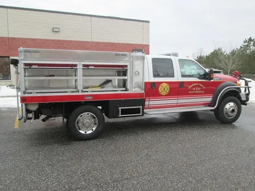 Exterior view of small fire truck showing cab, body compartments, and wheel/tire area.