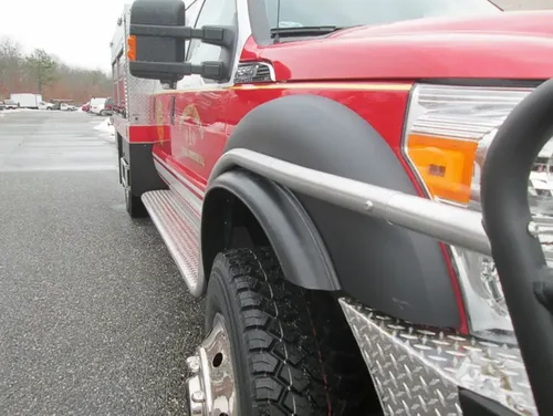 Exterior view of small fire truck showing cab, body compartments, and wheel/tire area.