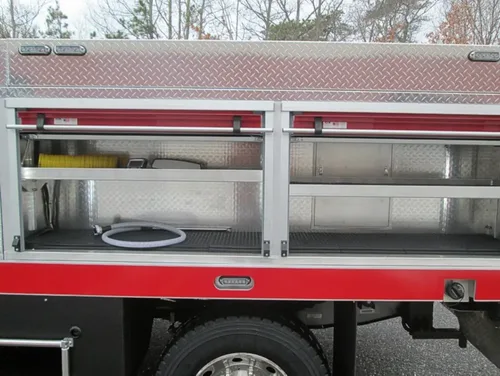 Exterior view of small fire truck showing cab, body compartments, and wheel/tire area.