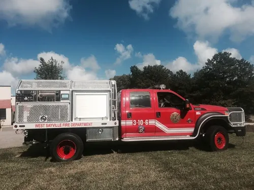 Exterior view of small fire truck showing cab, body compartments, and wheel/tire area.