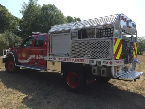 Exterior view of small fire truck showing cab, body compartments, and wheel/tire area.