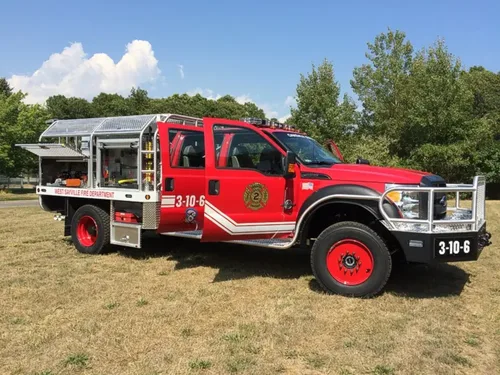 Exterior view of small fire truck showing cab, body compartments, and wheel/tire area.