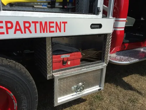 Exterior view of small fire truck showing cab, body compartments, and wheel/tire area.