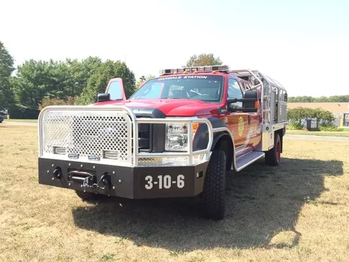 Exterior view of small fire truck showing cab, body compartments, and wheel/tire area.