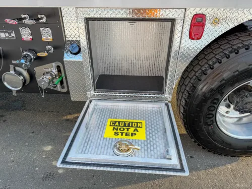 Lower side tank compartment open beside the pump panel and rear wheel.