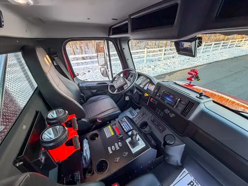 Interior side view with driver seat, steering wheel, and center console controls.
