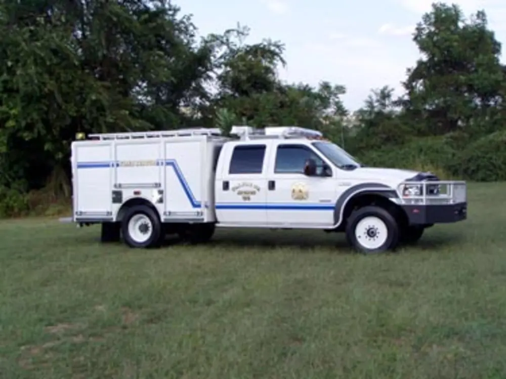 Exterior view of small fire truck showing cab, body compartments, and wheel/tire area.