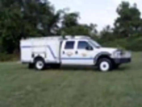 Exterior view of small fire truck showing cab, body compartments, and wheel/tire area.