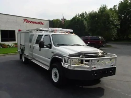 Exterior view of small fire truck showing cab, body compartments, and wheel/tire area.