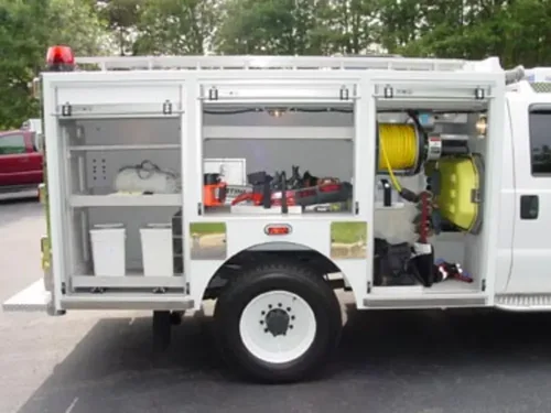 Exterior view of small fire truck showing cab, body compartments, and wheel/tire area.