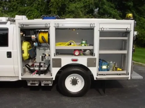 Exterior view of small fire truck showing cab, body compartments, and wheel/tire area.
