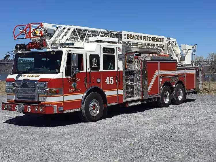 Front left exterior view of a rear-mount aerial ladder truck with tandem rear axles and stowed ladder.