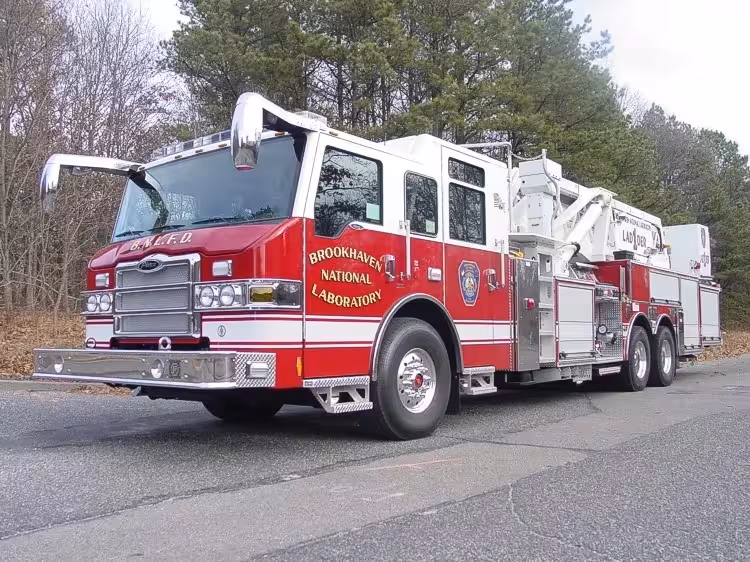 Front-left exterior view of a tower ladder showing the enclosed cab, ladder body, and tandem rear axles.