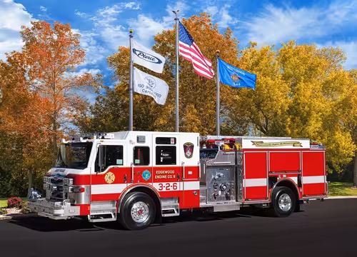 Driver-side profile of a pumper parked beneath flagpoles showing full side body and wheelbase.