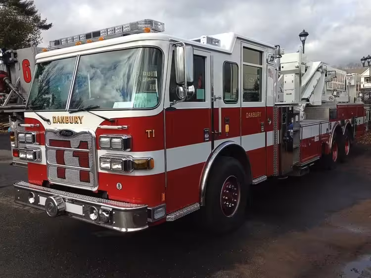 Front-left exterior view of tower ladder truck showing cab, ladder base, and tandem rear axles