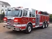 Wide front left angle of the parked apparatus with cab, bumper, and side body compartments.