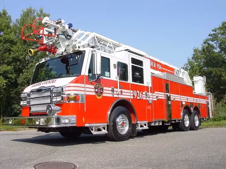 Front-right exterior view of a rear-mount aerial ladder with front outrigger, side compartments, and tandem rear axles.