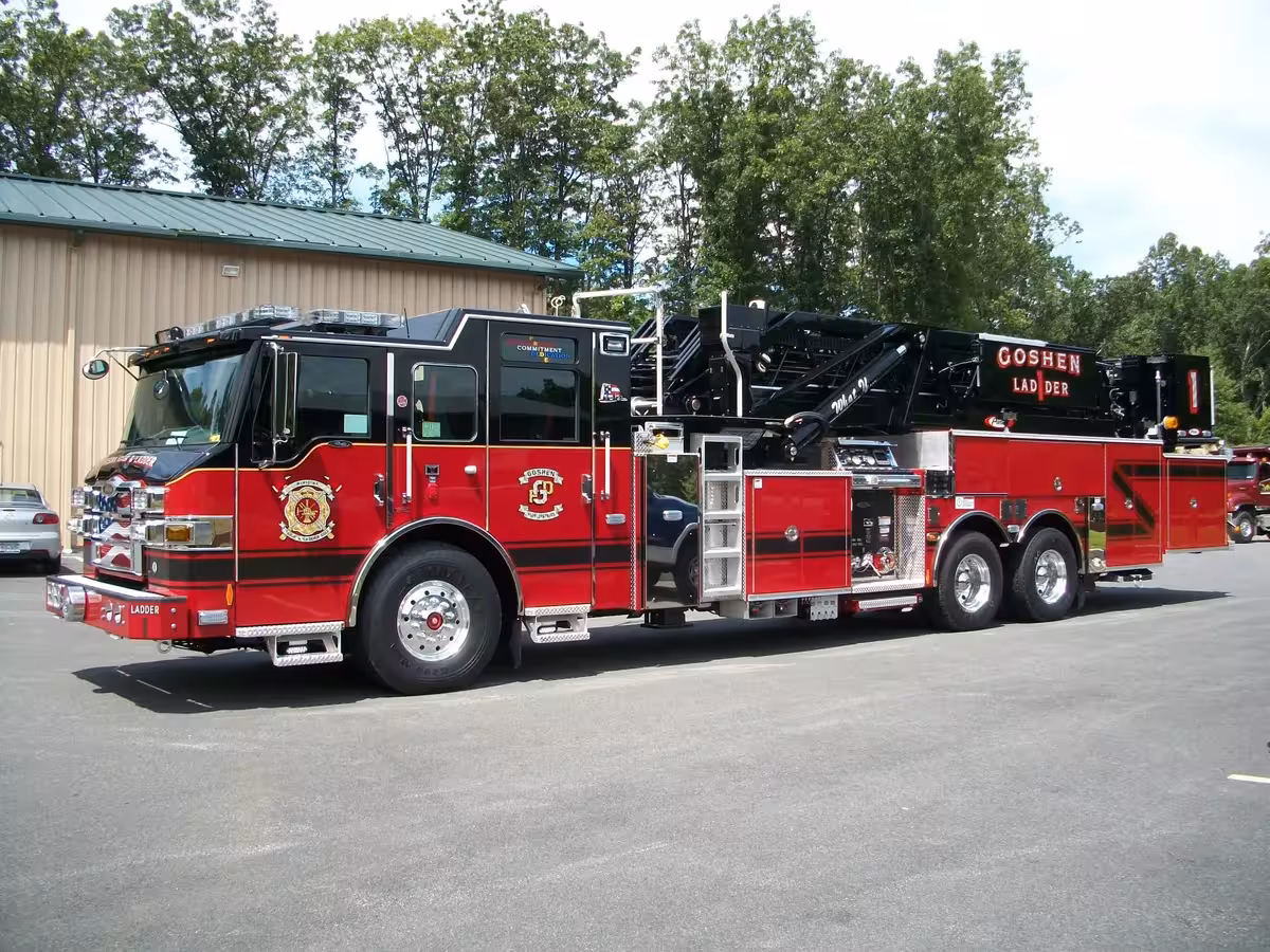 Driver-side full profile of a ladder truck with stowed aerial, side compartments, and tandem rear axles.