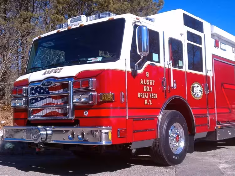 Front-left close view of a pumper showing the cab, grille, bumper, and driver-side body compartments.