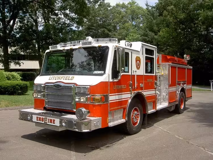 Front left exterior view of the pumper with chrome bumper, cab roof lights, and side body compartments.