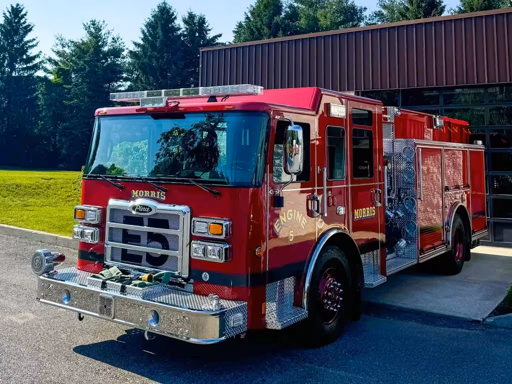 Front left exterior view of the pumper with chrome bumper, grille, pump panel side, and hosebed area visible.