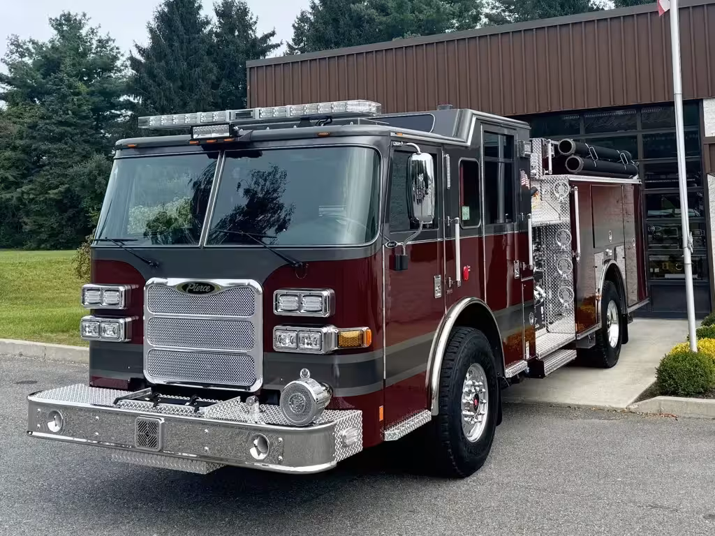 Front-right exterior view of a pumper showing the grille, bumper, cab, and side pump panel section.