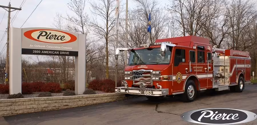 Front-left exterior view of a pumper parked beside a Pierce sign showing cab and side body profile.