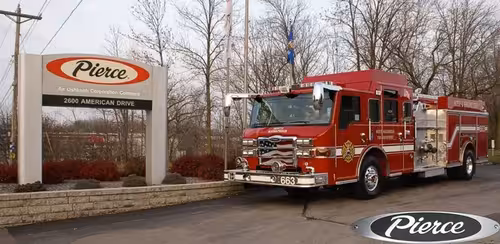 Front-left wide view of the pumper by the sign showing full cab and rear body compartments.