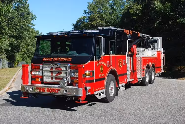 Front-left exterior view of a tower ladder with front outrigger deployed, side compartments, and tandem rear axles.