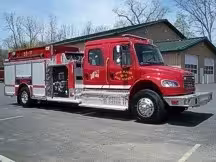 Wide driver-side three-quarter view of the pumper with commercial cab, pump panel area, and side compartments.