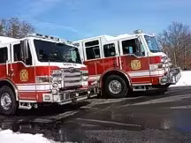 Wide side-front view of two red-and-white pumpers parked together on wet pavement.