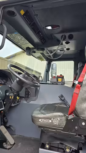 Driver cockpit view showing steering wheel, instrument cluster, and overhead switch panel