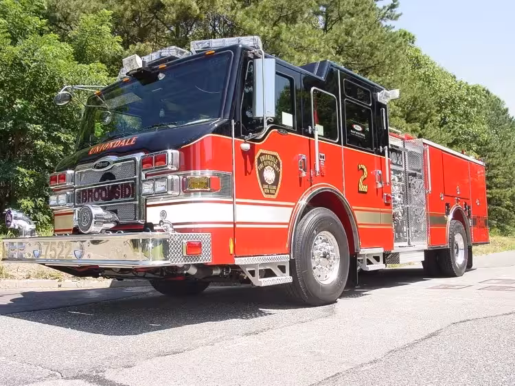 Front-left exterior view of a pumper showing the cab, side pump panel section, and rear body compartments.