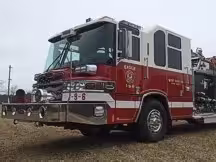 Wide front-left view of the pumper parked on grass with the cab and pump panel section visible.