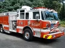Wide front-right view of the rescue pumper parked by the building with full side body visible.