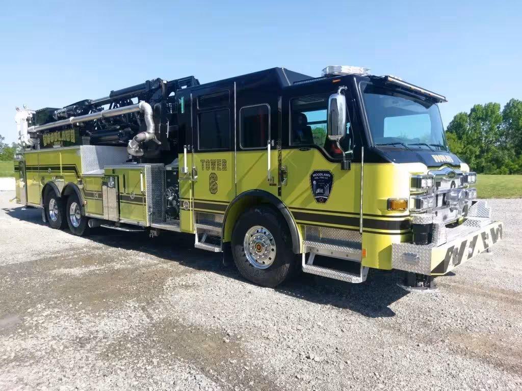 Tower ladder truck front-left exterior view showing enclosed cab and black ladder bed