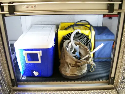 Open side compartment showing cooler, hose bundle, and utility storage