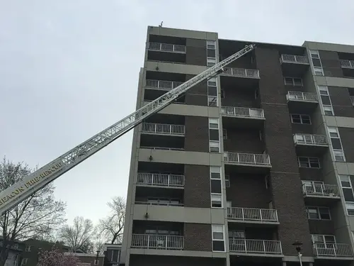 Extended aerial ladder reaching to an upper balcony level on a multi-story apartment building.