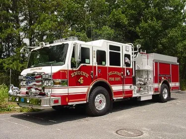 Front-right exterior view of a pumper showing the enclosed cab, bumper, and side body compartments.