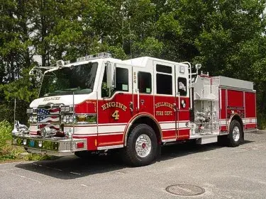 Front-right exterior view of a pumper showing the enclosed cab, bumper, and side body compartments.