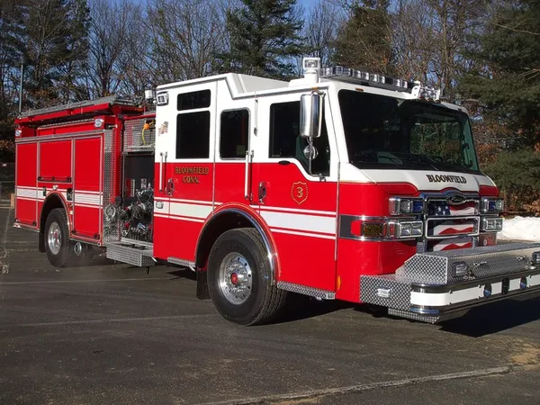 Front right exterior view of a red-and-white pumper with chrome bumper, crew cab, and side compartments.
