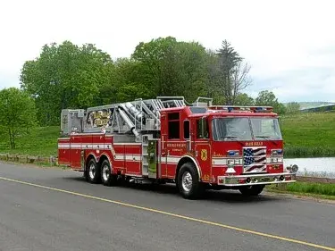 Front right exterior view of a mid-mount tower ladder with tandem rear axles and stowed aerial sections.