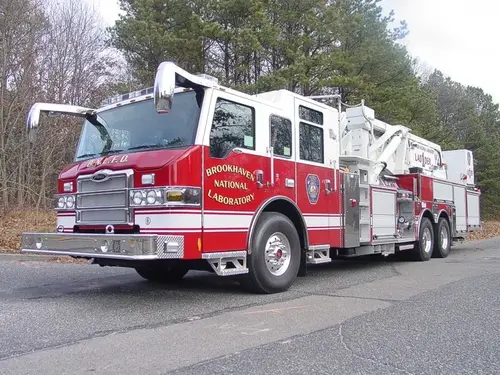 Front-left exterior view of a tower ladder showing the enclosed cab, ladder body, and tandem rear axles.