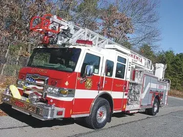 Front-right exterior view of a ladder truck with stowed aerial, side pump panel, and body compartments.