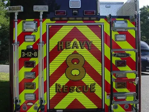 Straight rear view with red-yellow chevrons, rear warning lights, access ladder, and center rear roll-up door.