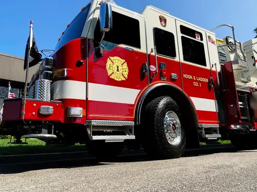 Pierce tower ladder low front-left view showing cab, front wheel, and tiller body