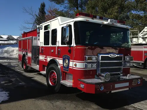 Front-right exterior view of a pumper with enclosed cab, side pump panel section, and body compartments.