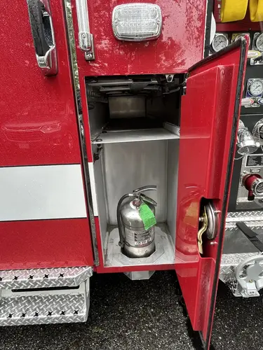 Narrow side compartment near pump panel showing mounted fire extinguisher and upper shelf